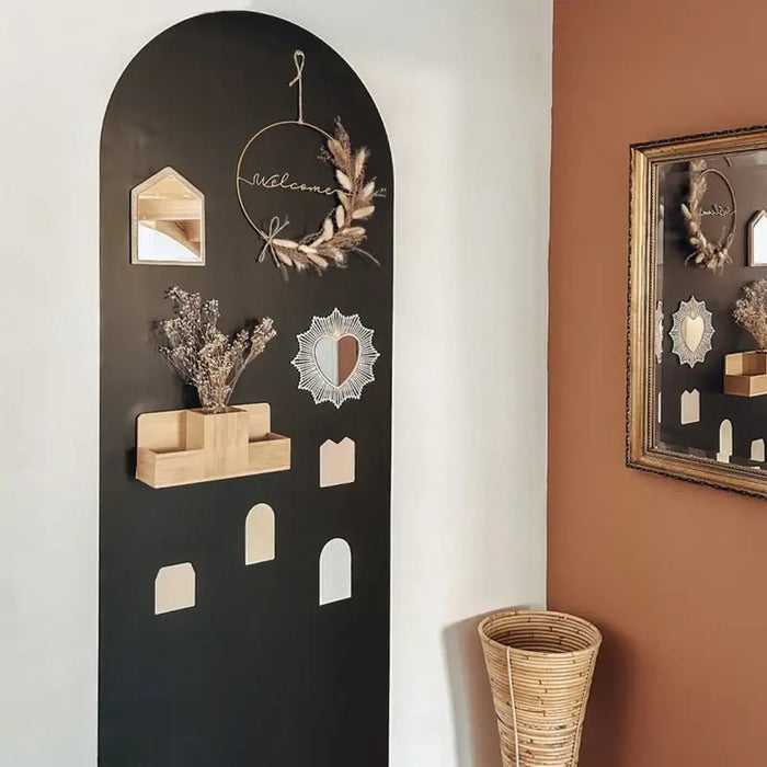 Tall, arched black magnetic wallpaper on a white wall decorated with a wooden shelf and small mirrors.