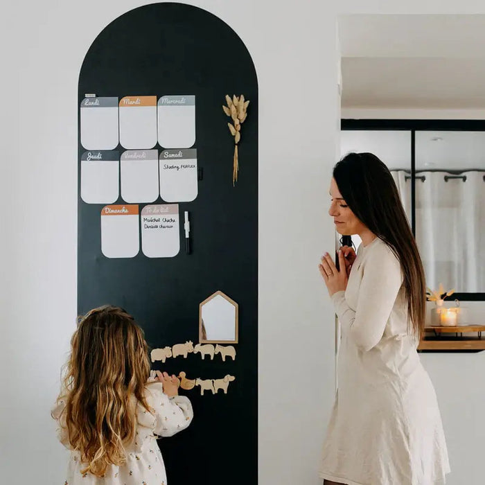 Tall black arched magnetic wallpaper with a weekly planner and animal magnets being used by a mother and child.