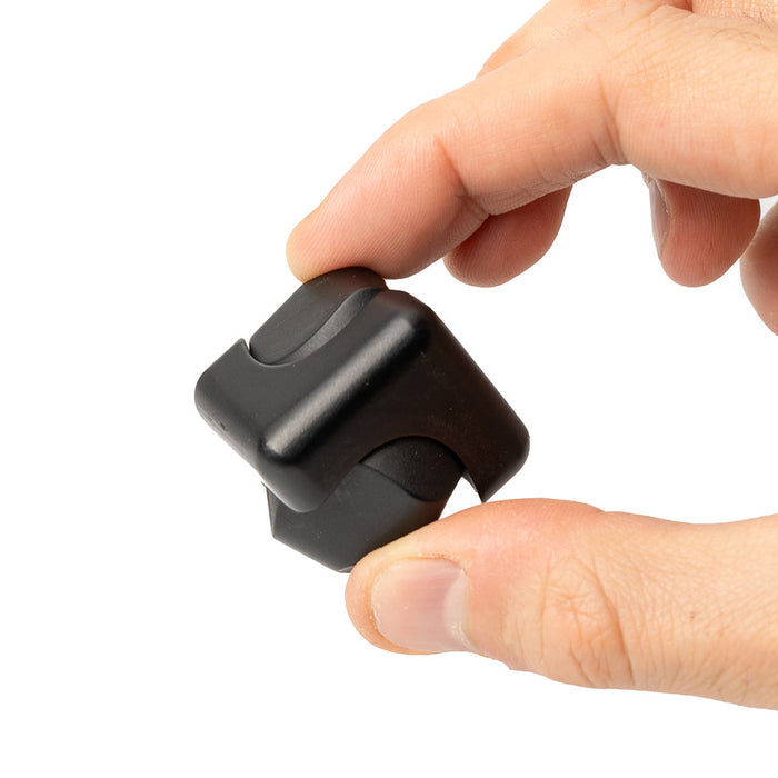 Hand holding a matte black interlocking metal fidget spinner cube against a white background.