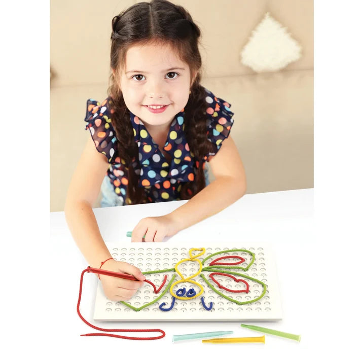Smiling girl uses a red stylus to thread colorful laces into a white pegboard to create a butterfly design.