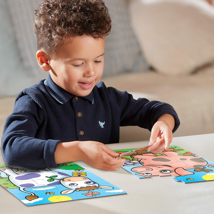 Smiling boy assembling large, colorful cow and pink pig jigsaw puzzles on a white table.