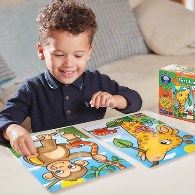 Young boy completes colorful monkey and giraffe jigsaw puzzles on a table next to the vibrant product box.