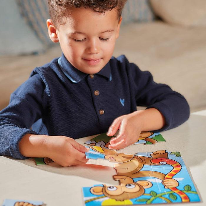A young boy assembling a vibrant monkey and snake jigsaw puzzle on a light-colored table.