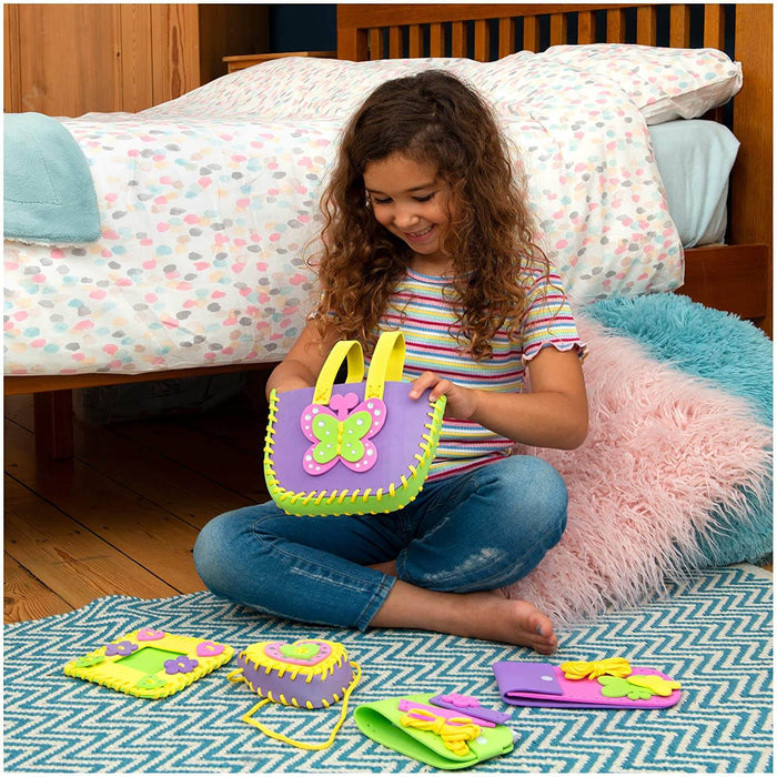 Child holding a purple and green felt butterfly bag with other colorful sewn craft projects on a rug.