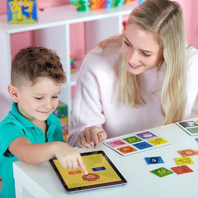 Young boy and teacher playing an interactive sound game with a tablet and colorful square animal picture cards.