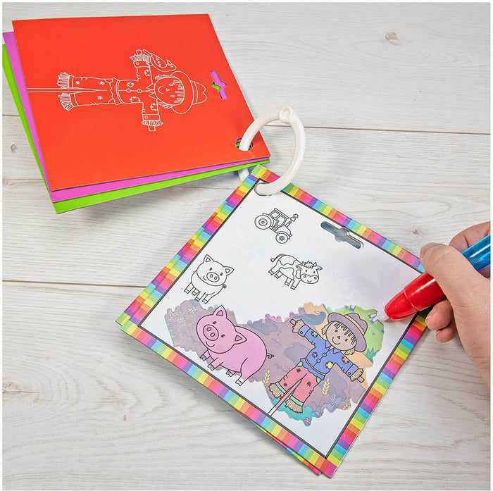 Hand using a red water pen to reveal a colorful farm scene with a pink pig and scarecrow in a ring-bound activity book.