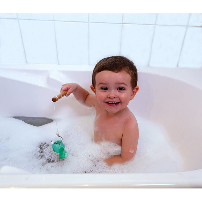 Smiling toddler in a bubble bath catches a green plastic toy fish with a wooden fishing rod.