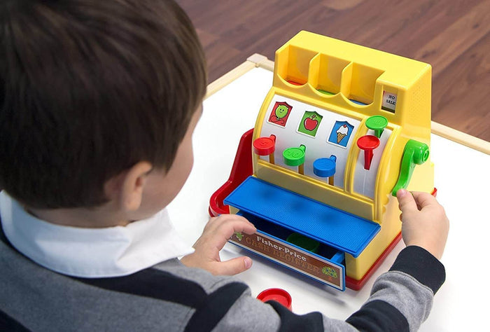 Child operating a yellow toy cash register with colorful buttons, food icons, a blue drawer, and a green side crank.
