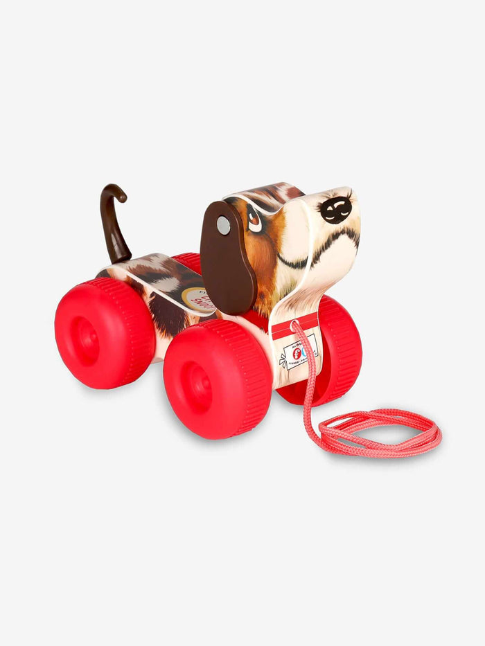 Wooden toy dog with brown and white patterns, floppy ears, chunky red wheels, and a red pull string.
