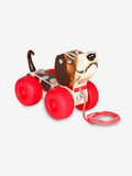 Wooden toy dog with brown and white patterns, floppy ears, chunky red wheels, and a red pull string.