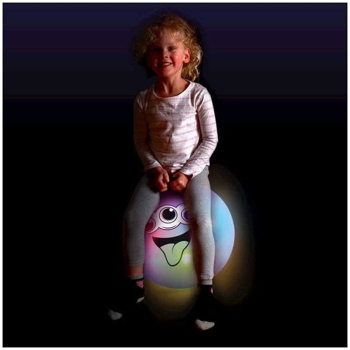 Child sitting on a glowing translucent inflatable ball with a cartoon alien face, set against a black background.