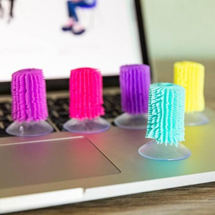 Five colorful, bristly suction cup toys in pink, purple, teal, and yellow standing on a silver laptop.