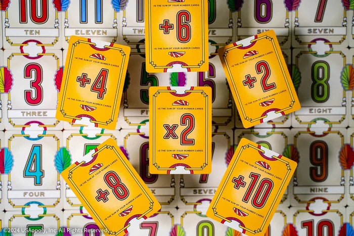Yellow cards with math modifiers like +10 and x2 layered over white cards featuring large, colorful numbers.
