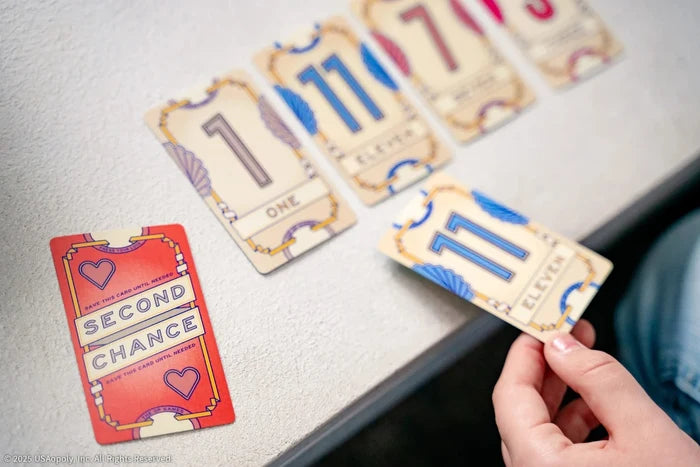 Hand placing an 11 card next to cards numbered 1 and 7, and a red Second Chance card on a white background.