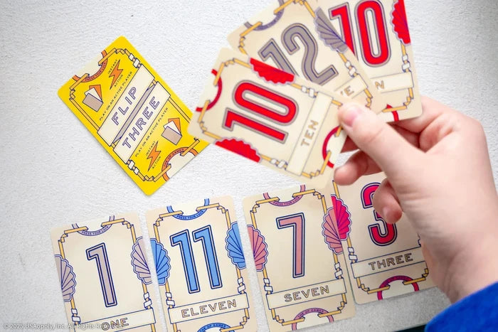 Hand holding colorful numbered cards over a table spread of Art Deco style cards in red, blue, purple, and yellow.