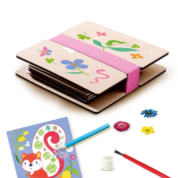 Wooden flower press with nature illustrations, pink strap, dried flowers, paintbrush, and a colorful fox craft card.