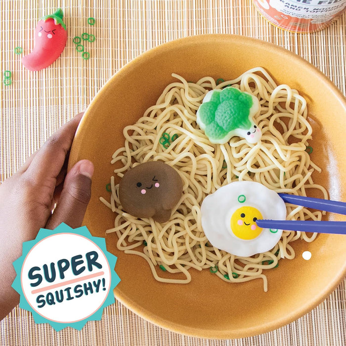 Toy ramen bowl with noodles, blue chopsticks, and squishy toppings including a smiling broccoli, egg, and mushroom.