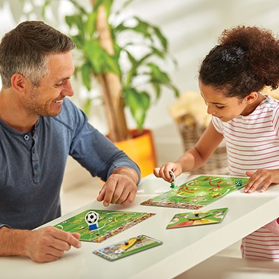 Man and girl play a football board game with green field boards, cardboard player pieces, and a spinner on a white table.