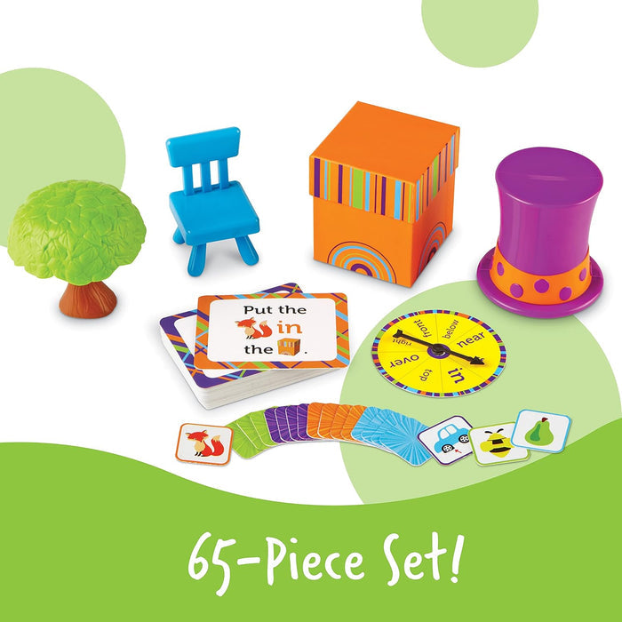 Colorful preposition toy set with a green tree, blue chair, orange box, purple hat, spinner, and cards.