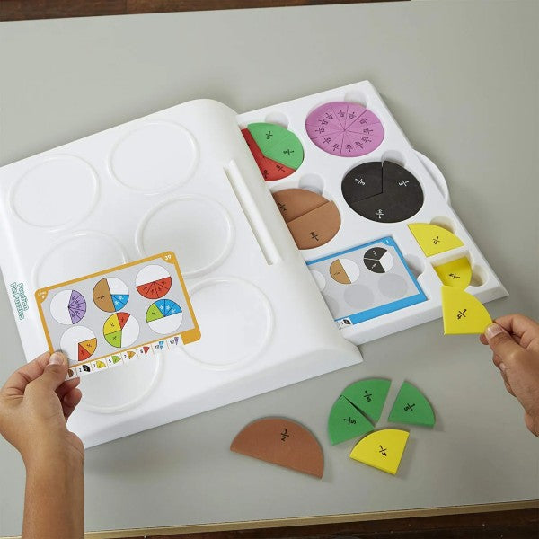 White tray with circular slots, colorful fraction wedges, a challenge card, and hands holding a yellow piece.