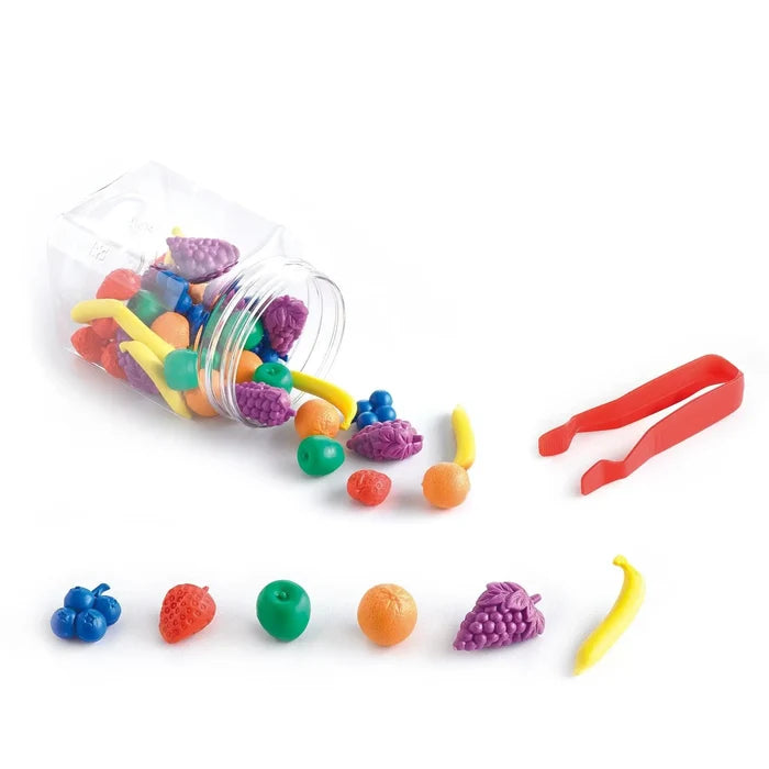 Colorful plastic fruit counters spilling from a clear jar next to red tweezers and a sample row of fruit shapes.