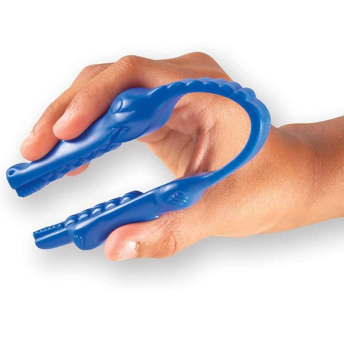 A child's hand squeezing a blue alligator-shaped plastic tweezer tool with textured finger grips and snout.