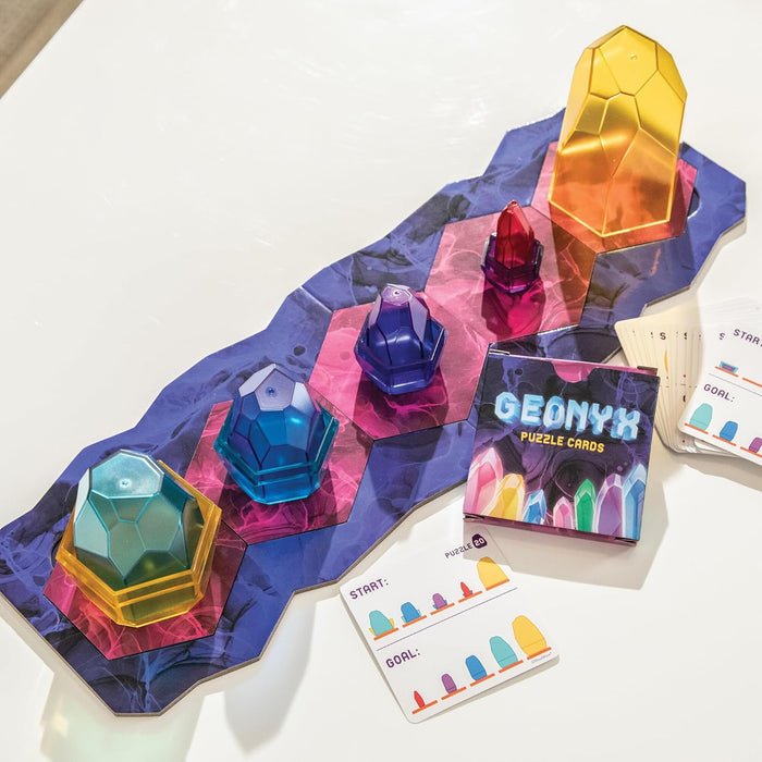 Five colorful, faceted translucent gems on a purple hexagonal game board with puzzle cards and a small box.