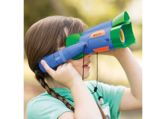 Child using blue and green plastic binoculars with integrated headphones and orange accents while looking outdoors.