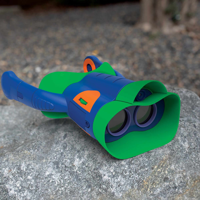 Blue and green toy binoculars with orange accents and oversized eyepieces, resting on a textured grey rock.