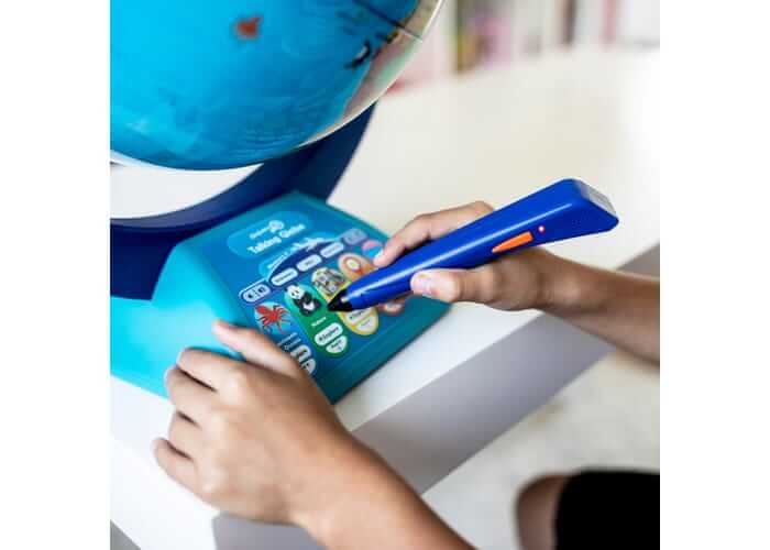 Child using a blue electronic pen to touch colorful buttons on the base of a bright blue interactive globe.