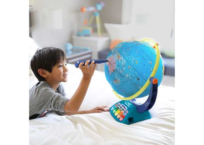 A boy using a blue stylus to explore a bright blue world globe with a colorful, button-filled base.