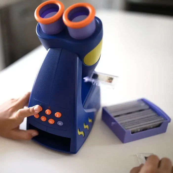 Child's hand on a blue toy microscope with orange eyepieces and buttons next to a tray of slides on a white surface.