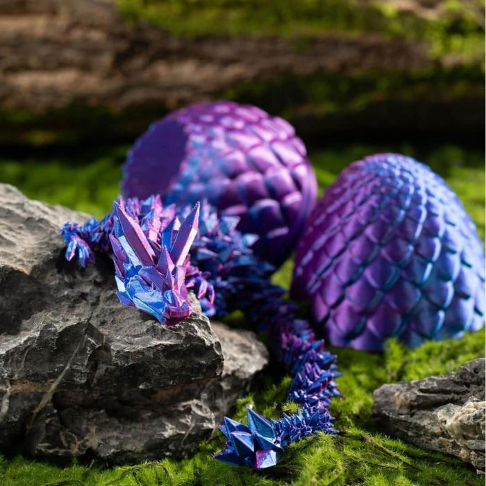 Iridescent purple and blue 3D printed crystal dragon and matching scaly eggs on moss and rocks.