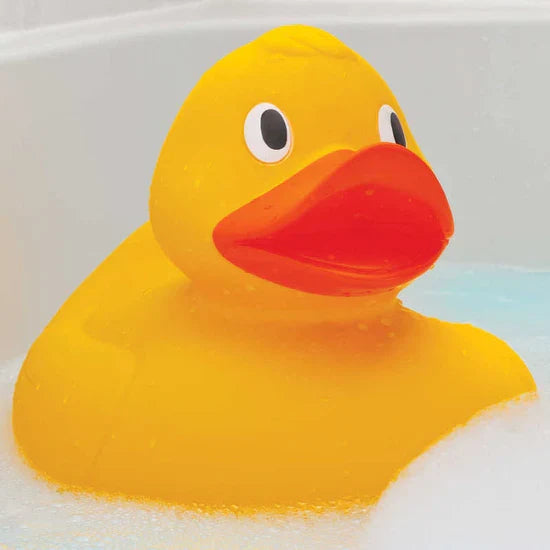 Large yellow rubber duck with a bright orange beak and big eyes floating in soapy bath water.