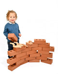 Child building a wall with large terracotta-colored foam bricks and wooden toy trowels.
