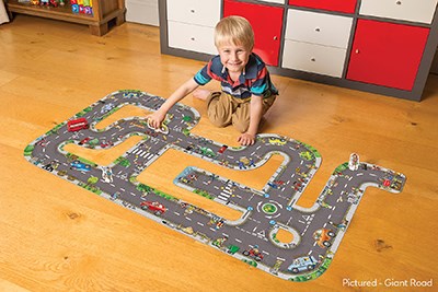 Young boy playing with a toy car on a large winding grey road floor puzzle with colorful illustrations.