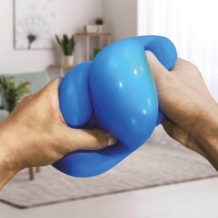 Two hands squeezing and stretching a large, bright blue squishy ball in a blurred living room setting.