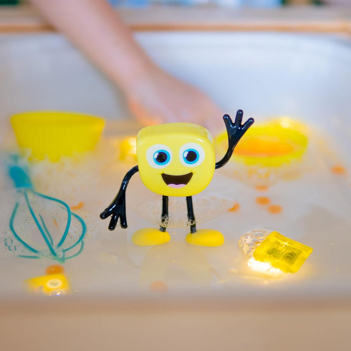 Yellow cube-shaped character toy waving in a water sensory bin with glowing cubes and a blue whisk.