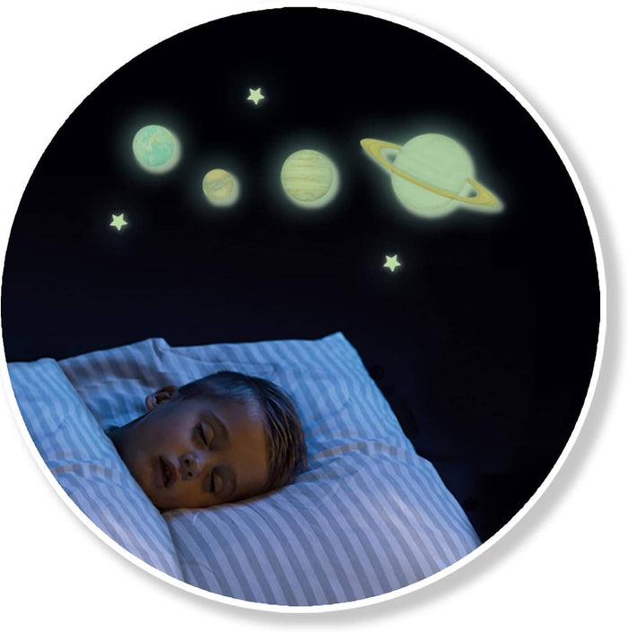 Child sleeping on striped bedding under glowing green planet wall stickers including Earth and Saturn with rings.