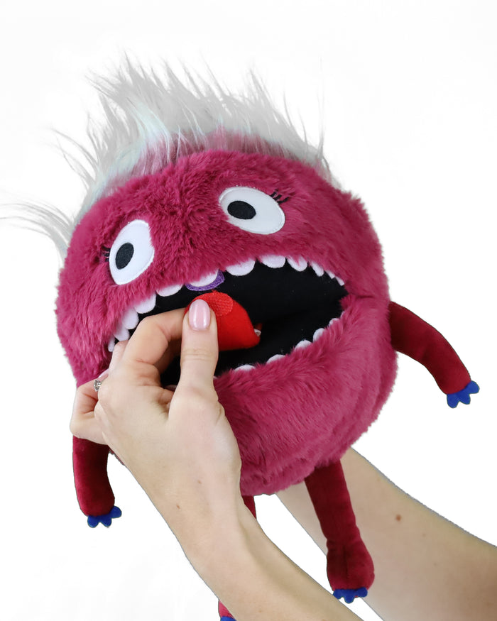 Pink fuzzy round monster puppet with white hair. A hand moves the red tongue inside its large, toothy mouth.