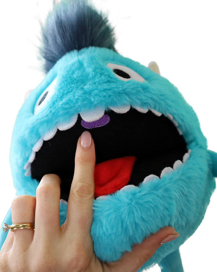 Fuzzy blue monster puppet with an open mouth. A finger points to a purple uvula above a red tongue and white teeth.