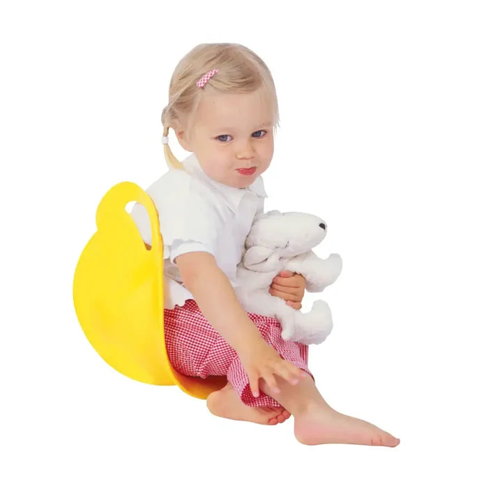 Toddler sitting in a bright yellow, rounded scoop-shaped spinner toy while holding a white plush lamb.