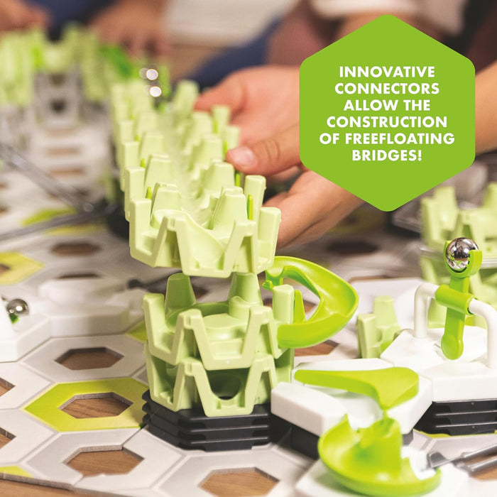 Hands stacking lime green plastic bridge components on a hexagonal baseplate to build an elevated marble run track.