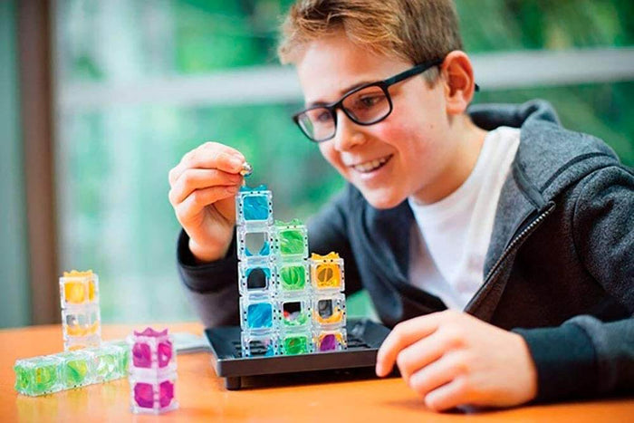 Boy drops a marble into a tower of colorful translucent cubes on a black game tray.