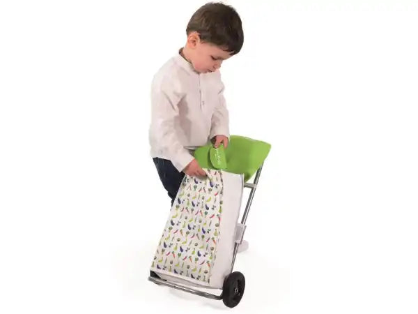 Toddler using a toy shopping trolley with a white fruit-print bag, lime green handle, and silver metal frame.