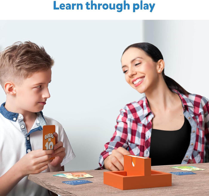 A boy and woman play Guess in 10 with colorful cards and an orange game stand on a wooden table.