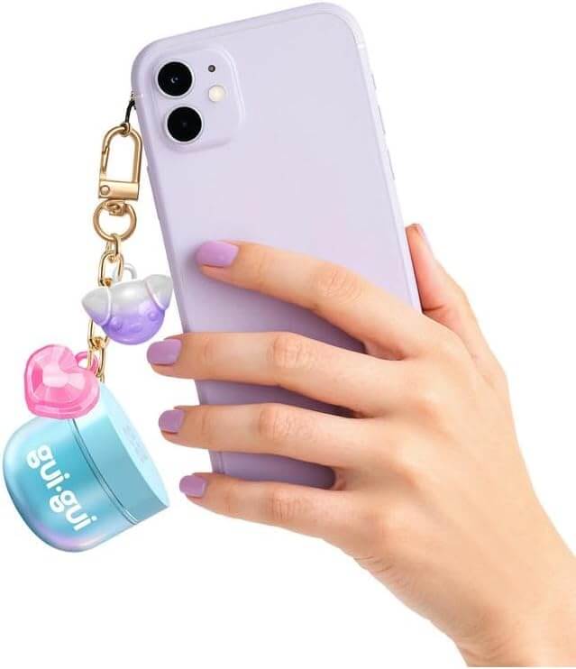 Hand holding a purple phone with a gold keychain featuring a purple dog, pink heart, and blue gradient mini slime jar.