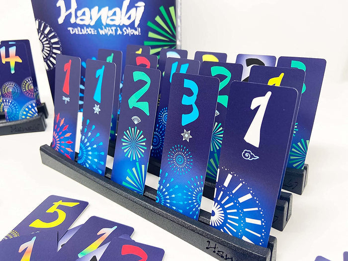 Tall blue cards with large colorful numbers and firework graphics standing in a black rack for Hanabi Deluxe.
