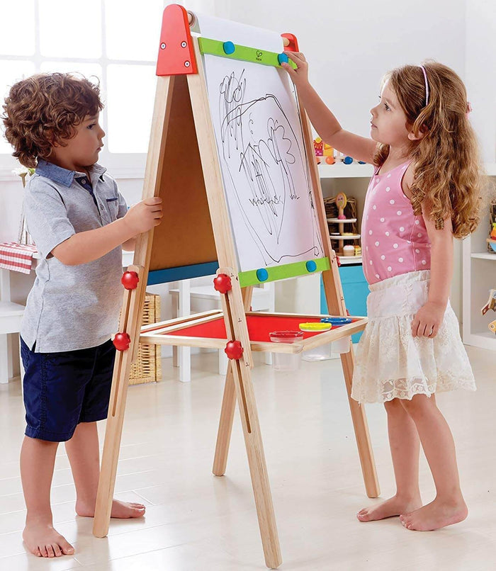 Boy and girl using an adjustable wooden easel with a paper roll, whiteboard, and red tray for paint cups.
