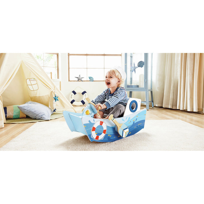 Blue wooden rocking boat toy with wave graphics, a life ring, and oars, featuring a toddler sitting inside.